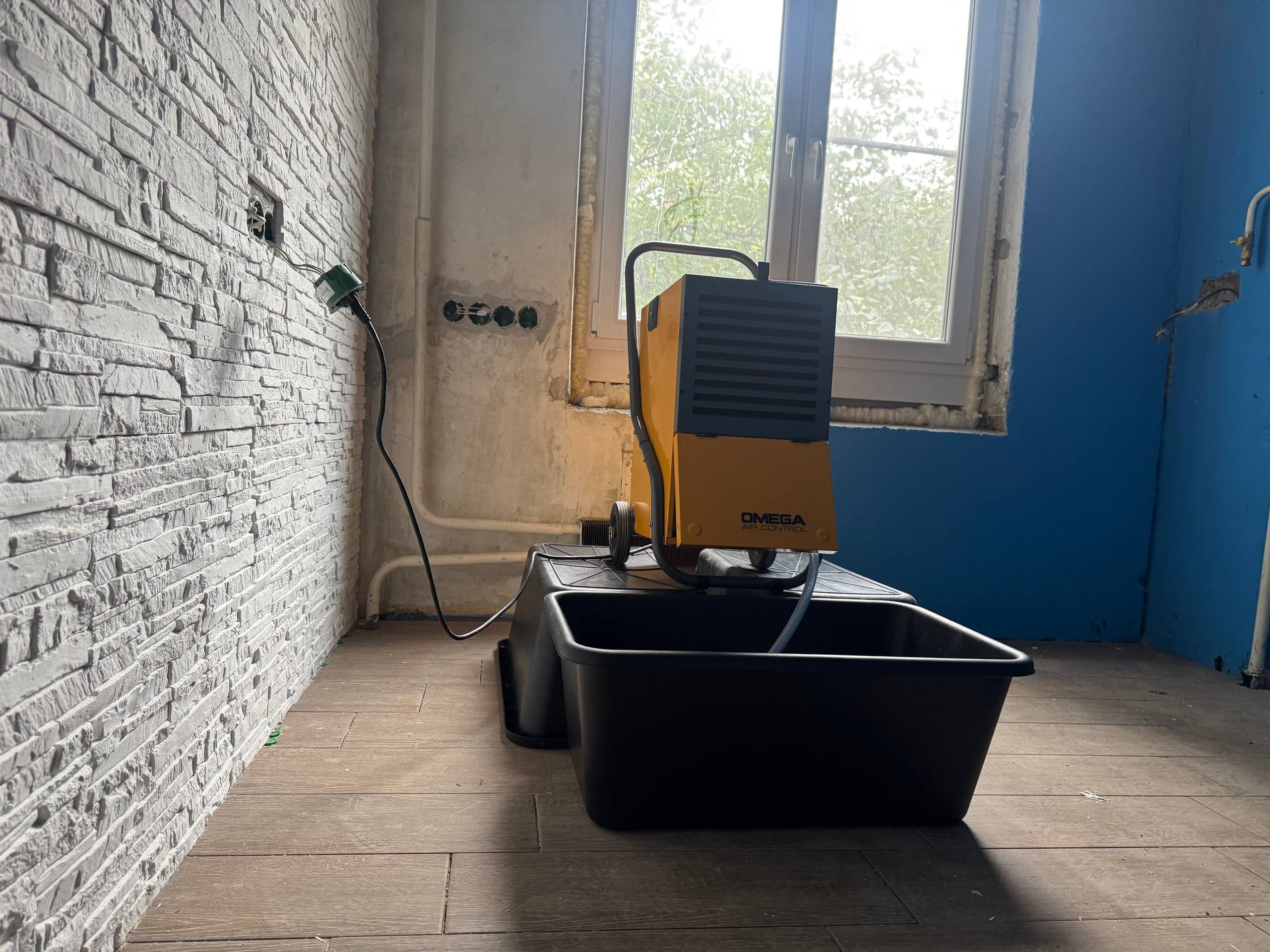 Осушитель у окна рядом с чёрными ёмкостями для сбора воды